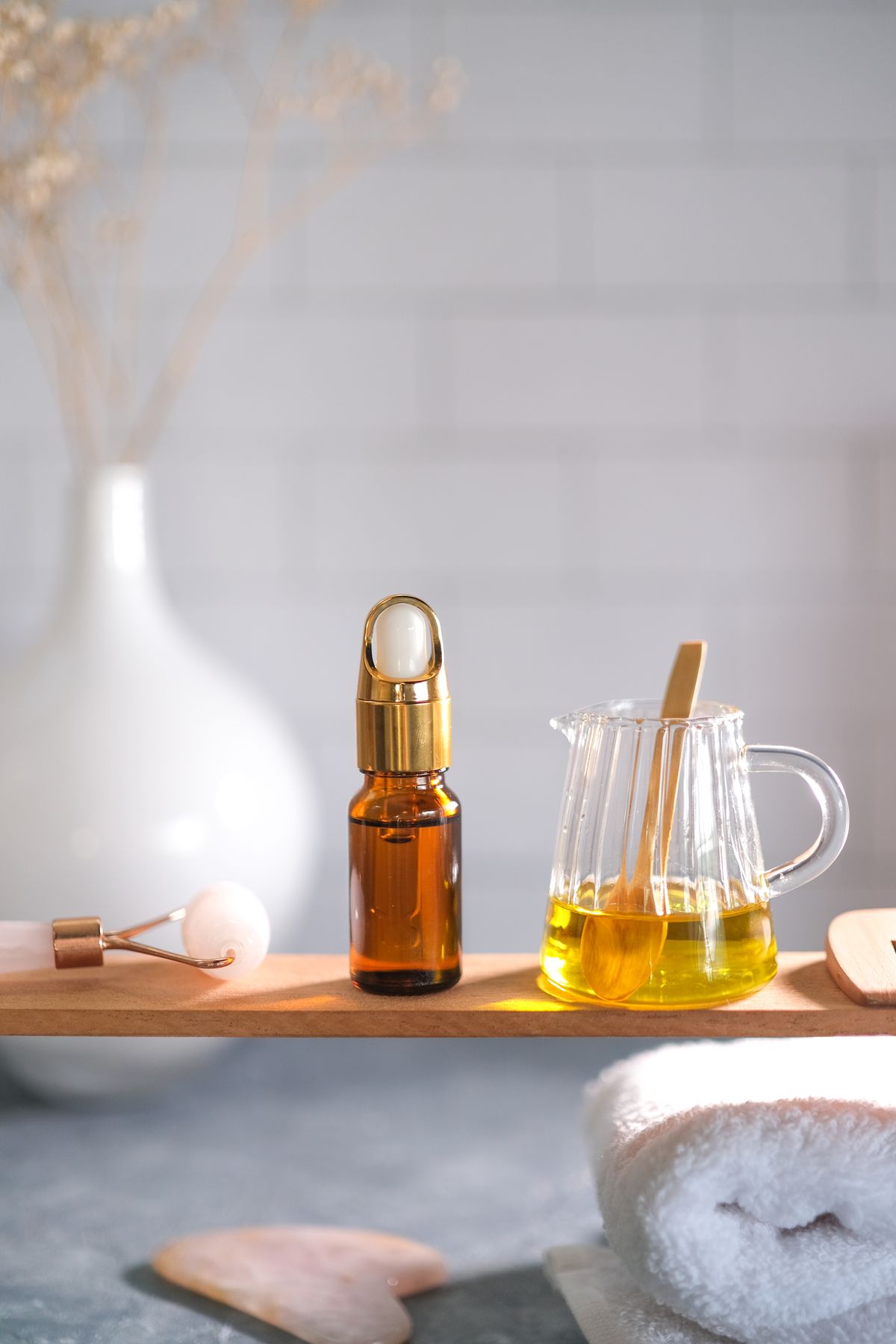 Flacon ambré, huile dorée et accessoires de soin disposés dans une lumière naturelle douce.