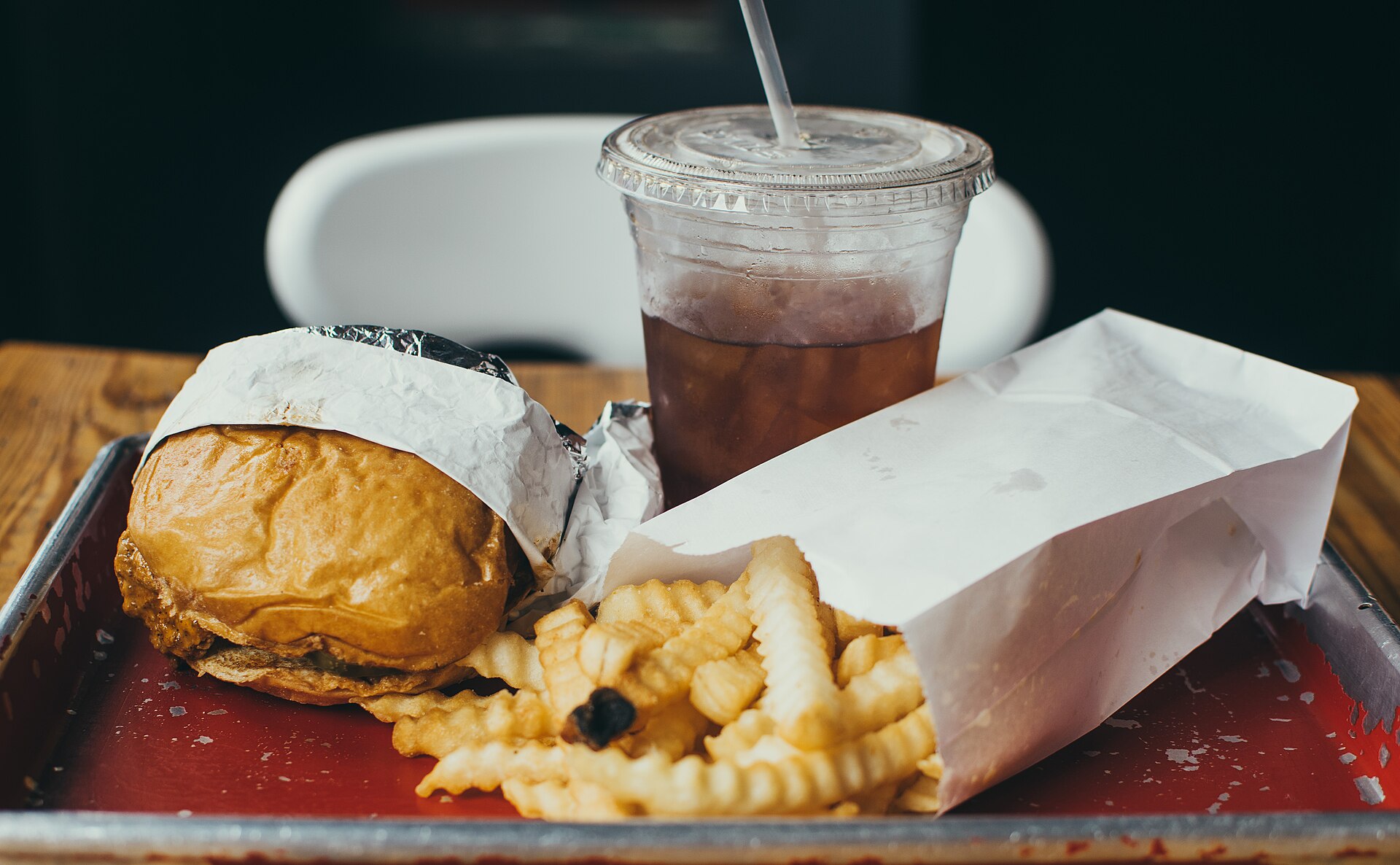 Plateau de service rouge : burger emballé dans son papier, frites ondulées débordant d'un sachet et gobelet glacé.