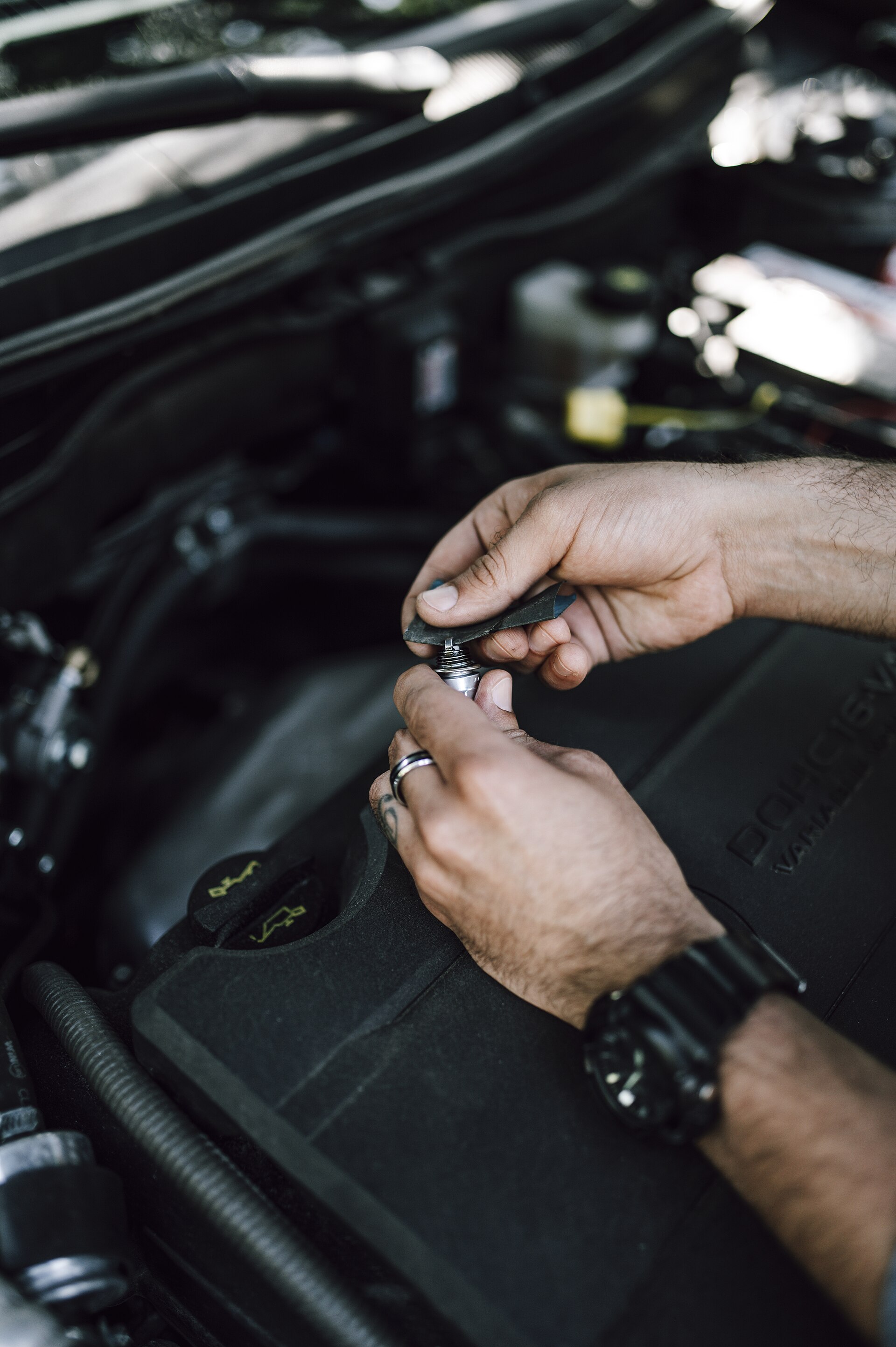 Mains gantées d'un mécanicien extrayant une bougie d'allumage du cache-culbuteurs d'un moteur