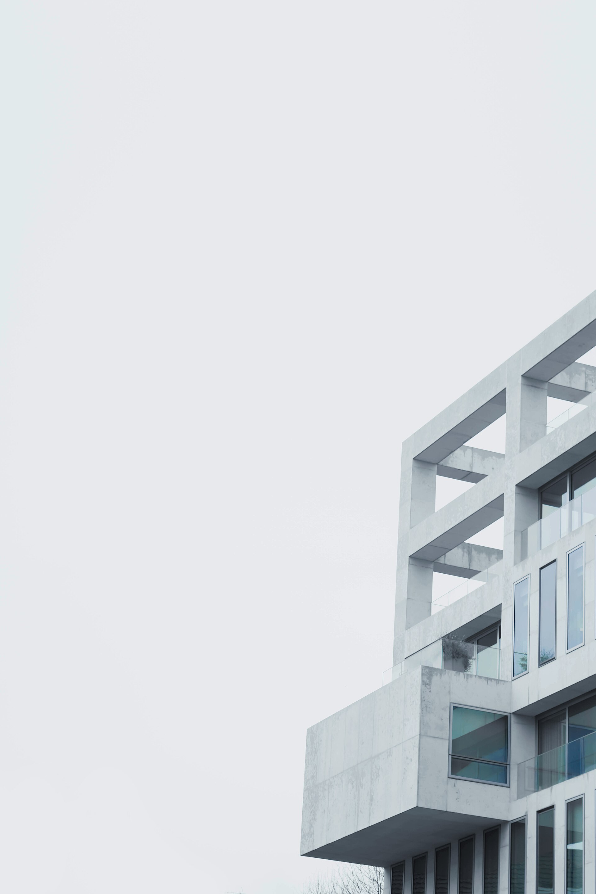 Bâtiment contemporain en béton clair vu en contre-plongée : portiques et terrasses dessinent une géométrie nette sur un ciel blanc.