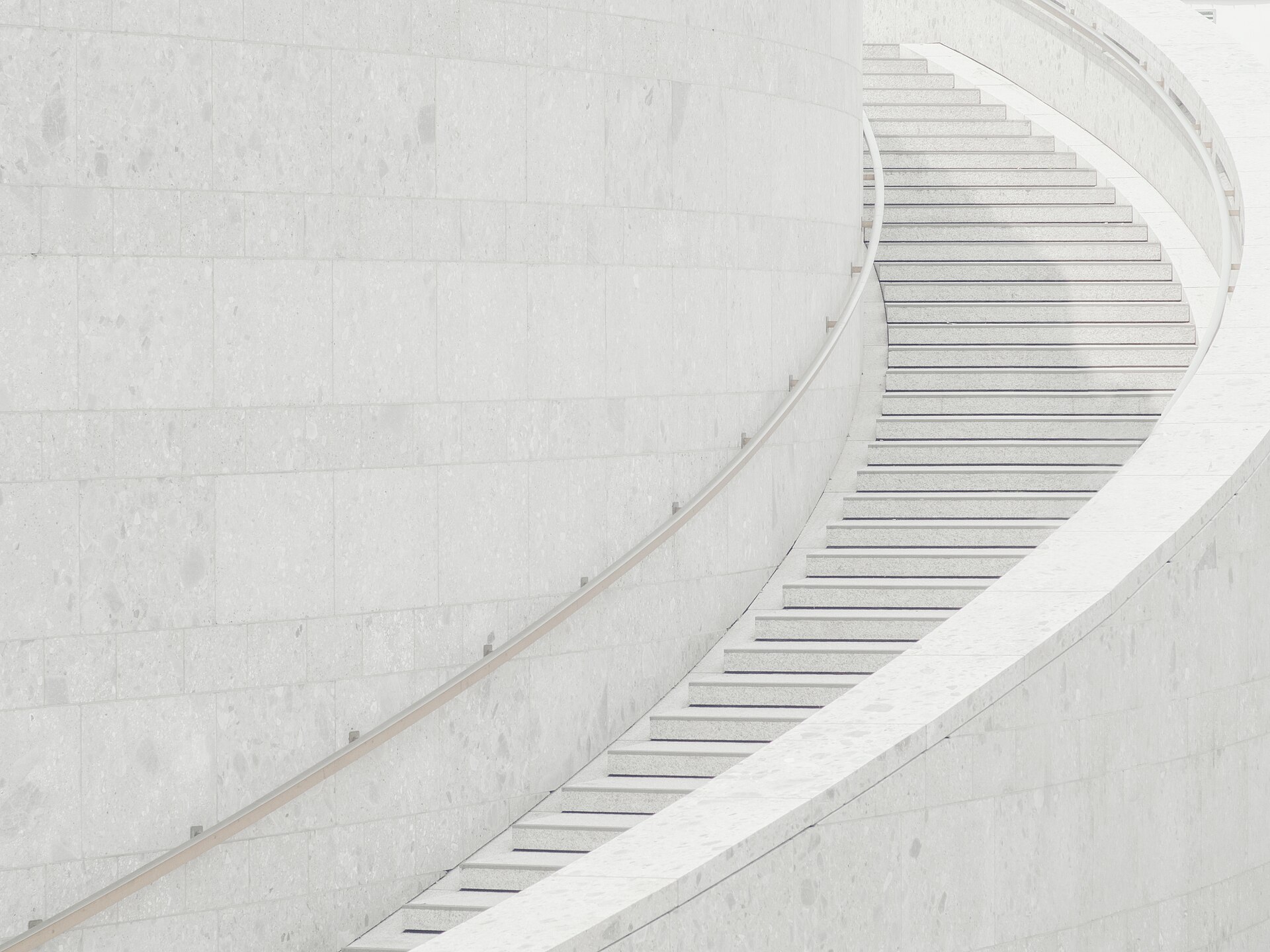 Escalier de béton clair décrivant une large courbe régulière le long d’un mur nu.