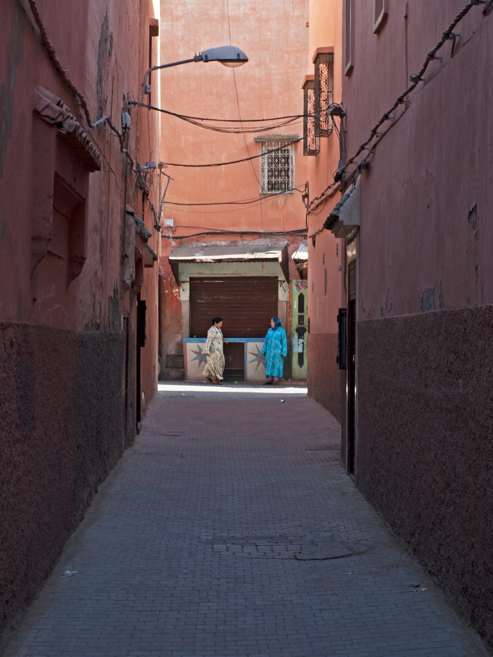 Ruelle étroite de la médina de Marrakech bordée de murs ocre, de portes sombres et de lanternes murales.