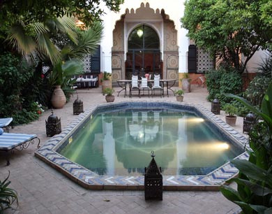 Patio de riad avec bassin rectangulaire et pavillon couvert sous une arcade.