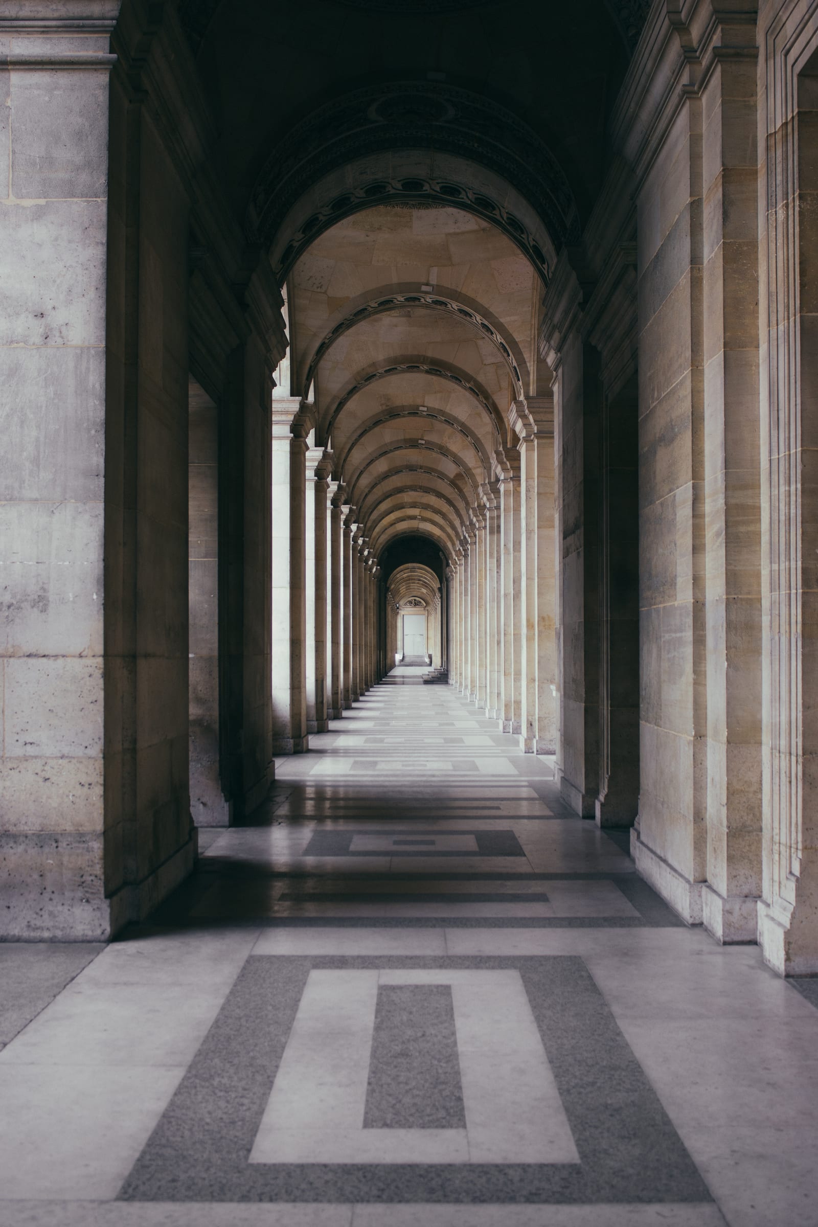 Galerie d'arches en marbre clair se répétant en perspective, sol réfléchissant.