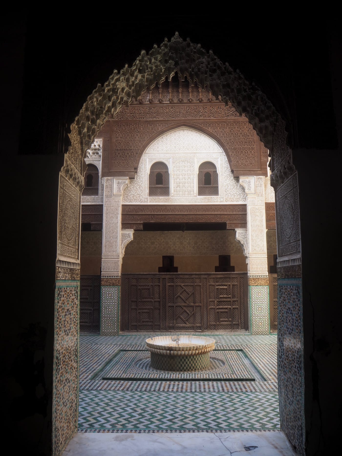 Grande arche marocaine sculptée ouvrant sur le patio lumineux d'une médersa à Meknès.