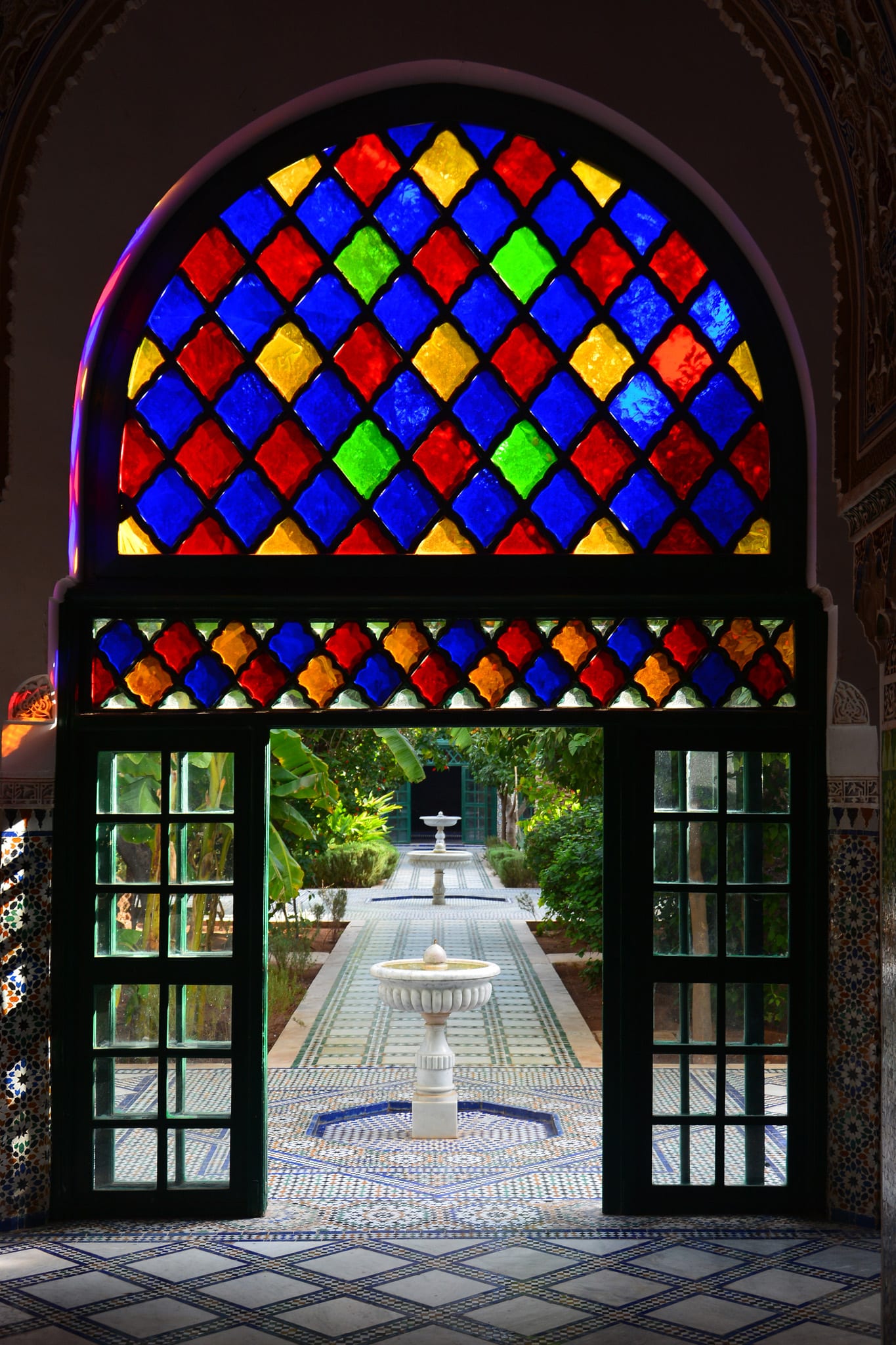 Porte à vitraux colorés ouvrant sur une cour du Palais de la Bahia, ses fontaines et ses mosaïques.