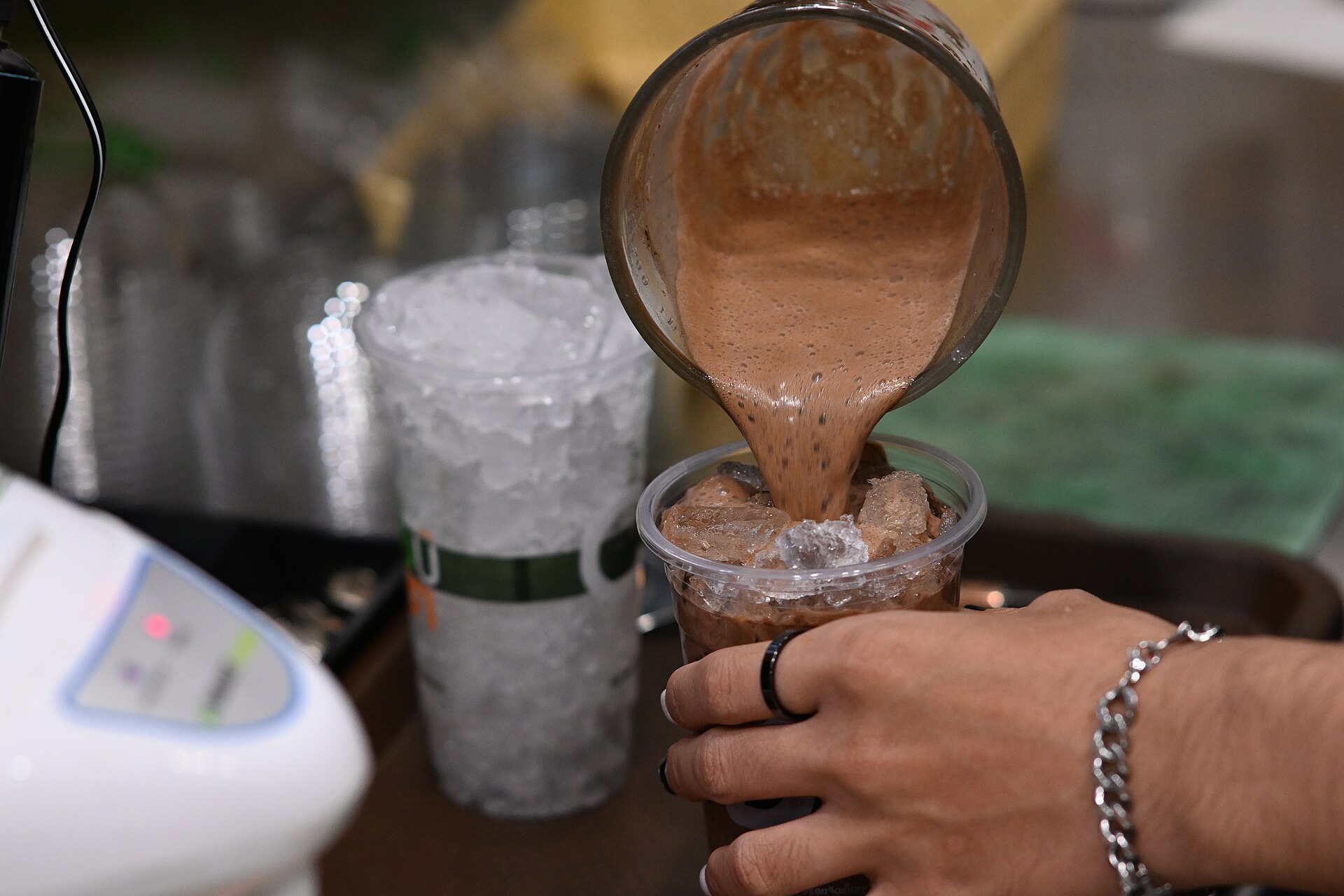 Milkshake au chocolat versé du bol du blender dans un gobelet rempli de glace, mousse épaisse en pleine coulée.